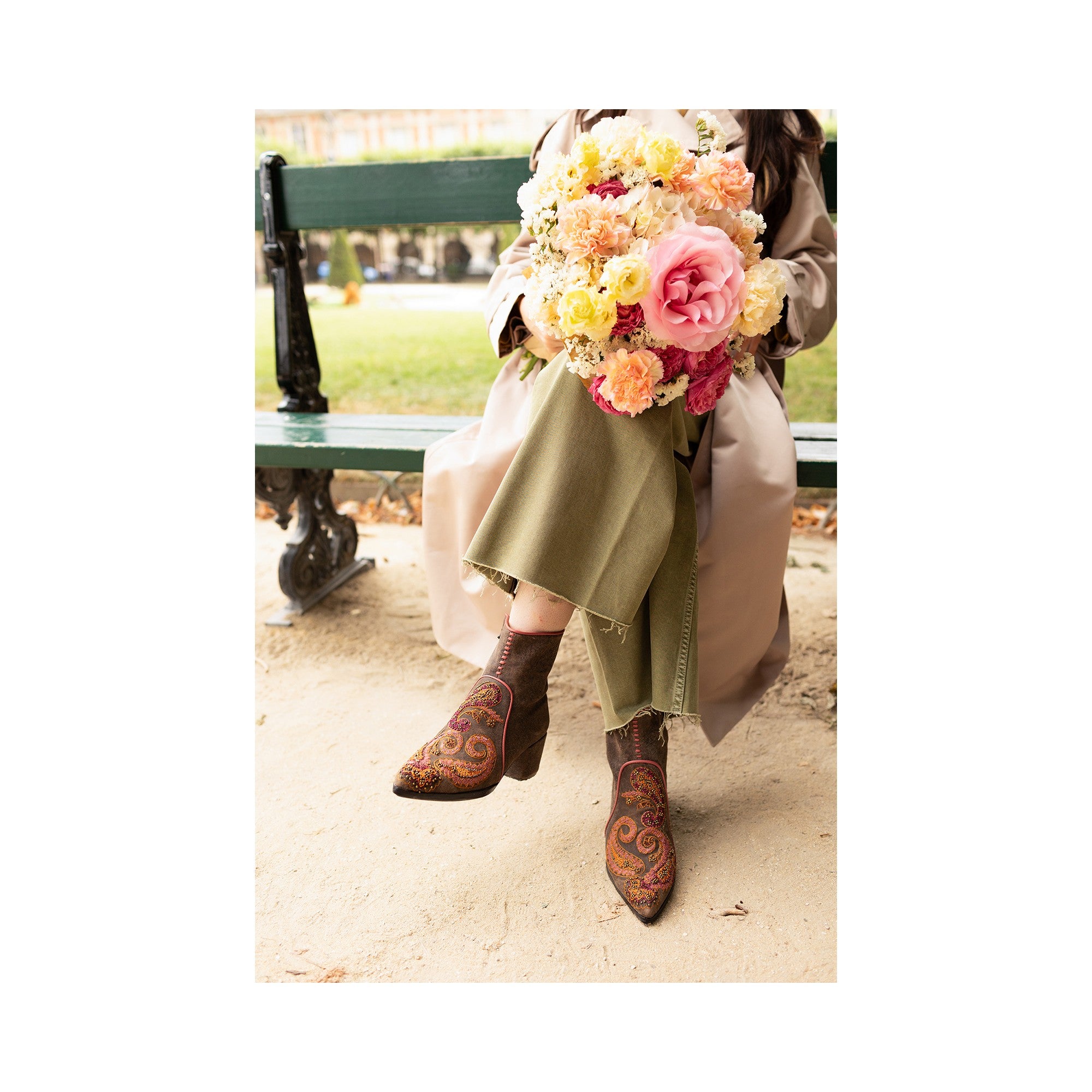 Handmade brown suede paisley-embroidered boots, paired with casual trousers and a floral bouquet, showcasing boho style.